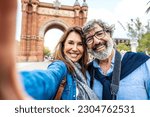 Small photo of Married couple taking selfie in front of Triumphal Arch in Barcelona, Catalonia, Spain - Husband and wife enjoying romantic moment together at summer holiday in Europe