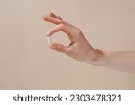 Female hand holding white pill with fingers on beige isolated background. Concept of health care, dietary supplements, treatment of depression and diseases