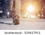 Winter macro photo of  woman boots. Girl walking in city park evening. Closeup photo of winter shoes. Blurred lens flare background with copy space area for a text. Snowfall in the wintry park.