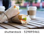 Chicken submarine sandwich from fresh baguette. Sandwiches with chicken, fresh vegetables and herbs on rustic wooden chopping board over wood backdrop, side view with coffee cup on background.