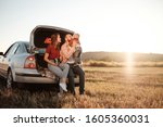Happy Young Family Mom and Dad with Their Little Son Enjoying Summer Weekend Picnic Sitting on the Trunk of the Car Outside the City in the Field at Sunny Day Sunset, Vacation and Road Trip Concept