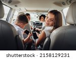 Cheerful Caucasian Teenage Girl Smiles Into Camera While Sitting in Minivan Car with Her Brother, Mother and Father, Happy Four Members Family Enjoying Weekend Road Trip