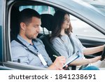 Small photo of Learning to drive a car. Male instructor and female student practicing in driving. Young man notice results of test in his paper. Cheerful woman satisfied with driving lessons.