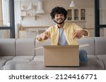 Small photo of Young smiling Indian man unpacking box with present sitting at home. Online shopping, delivery service concept. Successful blogger influencer recording video pointing fingers on carton box, copy space