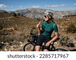 Small photo of Cyclist is resting.Female cyclist is wearing cycling kit holding energy snack for endurance during bicycle training.Sport nutrition.Sport snack for cyclist.Granola energy bar.