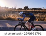 Male fit athlete riding time trial bicycle on empty road in golden hour. Sideview photo. Wearing helmet safety concept. Sport goal achieving. Extremely strong motivated person