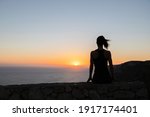 Backlit silhouette of a woman watching the sunrise over the sea