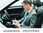 Businessman sitting in his car, he is planning and scheduling meetings on his organizer and using apps on his smartphone