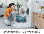Woman checking her damaged washing machine, the floor is flooded