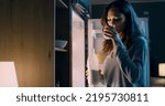 Small photo of Thirsty woman standing in front of her fridge and drinking a glass of milk late at night