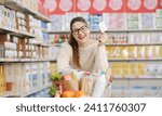 Small photo of Smiling customer leaning on a full shopping cart and showing a blank loyalty card at the supermarket, grocery loyalty program and discounts concept