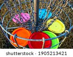 Disc golf basket with discs. The metal parts of the basket are selectively in focus.