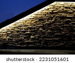 under the overhanging edge, lighting fixtures are placed under retaining wall and highlight relief of stone cladding at opera wall of hotel or airport railing. golden tones, city architecture, hidden
