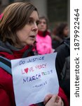 Small photo of New York City, New York, US - January 19, 2019: A white woman in a red coat with short brown hair holds a piece of paper that reads, "Do Justice, Love Mercy, March Proudly - Micah 6:8"