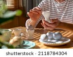 Small photo of Woman preparing colored easter eggs and painting eggcup for Easter holiday celebration.