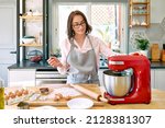 Small photo of Woman wearing apron baking cookies in a cozy kitchen. The housewife makes the dough for the cake in the planetary mixer. Homemade cakes or pies.