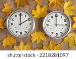 Small photo of For right-to-left readers: Two clocks, one shows two o'clock, the other shows three o'clock. Yellow fallen autumn leaves lie around. Symbol of time change. Moving the hands backwards from 3 to 2.
