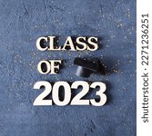 Small photo of Class of 2023 concept. Wooden number 2023 with graduated cap on dark concrete background with tinsel.