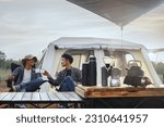Small photo of Asian young man two persons sitting enjoy coffee drink near a camping tent in the morning time, coffee drink relaxing on the morning summer camping vacation.
