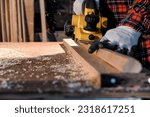 Small photo of Carpenter craftsman using electric hand wood planer making pool cue or snooker cue in carpentry workplace in an old wooden shed. Handmade craftsman concept. Selective focus on wood planing.
