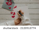 The girl writes a letter. Envelope with red hearts on a wooden background. Devushka writes a letter for her beloved