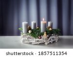 First advent with a burning candle on a wreath of white painted wood, fir branches and Christmas decoration against a purple-grey background, copy space, selected focus, narrow depth of field