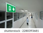 Small photo of Selective fire exit sign on white ceiling.Green fire escape sign hang on the ceiling in the office.Fire fighting equipment concept.