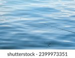 Small photo of A monofilament fishing line on a fishing rod ring against blue water. Fishing loat or bobber at the surface of the water.