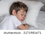 Small photo of The child is fast asleep lying with his head on a white pillow. Portrait of a white Caucasian 9-year-old boy in a white T-shirt