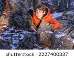 Small photo of Portrait of a boy (8 years old, white, Caucasian) sanctified by the rays of the sun hiding behind a stone in the mountains in the winter forest during a break between games