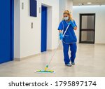 A cleaning lady with a mask on her face cleans the hallway