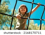 A child climbs up an alpine grid in a park on a playground on a hot summer day. children