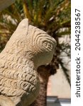Small photo of Detail of an sculpture of a replica of a lion or the fount of the lions of the Alhambra of Granada in the city of Arjona, in Jaen. In a blurry background a palm tree.