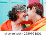 Happy gay senior lesbian couple wearing lgbt rainbow flag outdoors - Diversity family love - Main focus on right woman head