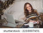 Portrait of smiling woman working on laptop or shopping online, buying new year presents with decorated Christmas tree on background, typing on keyboard. High quality photo