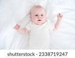 Small photo of healthy smiling baby lies on his back on bed on white bedding. top vie.