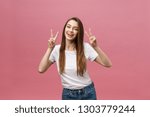 Small photo of Portrait of a cheerful trendy woman showing two fingers sign over pink background
