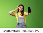 Small photo of Cute carefree asian brunette showing application on smartphone screen, make victory peace sign, smiling joyfully, brag social media popularity, followers amount, stand green background