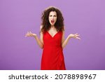 Woman being shocked guy breaking up with her during party. Concerned pissed and outraged good-looking lady in red dress with evening makeup shrugging with spread palms in clueless and questioned pose