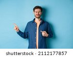 Small photo of Disappointed and skeptical guy frowning, pucker lips and pointing fingers left at empty space, complaining at bad thing, standing upset on blue background