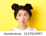 Small photo of Close-up of teen asian girl pucker lips and looking funny at camera, standing with glamour makeup and stylish hairstyle, yellow background