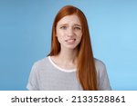 Small photo of Displeased young awkward redhead girl cringe full disbelief smirking frowning confused look questioned doubtful hearing nuisance dumb story standing blue background uncertain