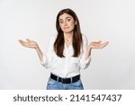 Small photo of I dont know. Clueless young woman shrugging shoulders and looking unaware, standing over white background