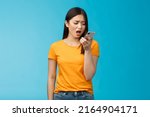 Small photo of Upset whining displeased moody girlfriend complaining talk into smartphone hold phone near mouth upset, frowning bothered bad connection, record voice message, blue background