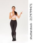 Small photo of Full length of sassy attractive female athelte, asian fitness girl in sportswear pointing fingers upper right corner, demonstrating promo, showing workout equipment sale, fitness training discount