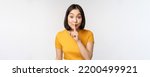 Small photo of Keep quiet. Cute asian woman make shhh gest, showing shush, hush sign, press finger to lips, silence, standing over white background