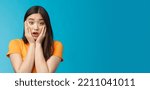 Small photo of Close-up concerned shocked young timid asian girl gasping, dropping jaw feel sorry, pitty for friend open mouth stunned stare camera, grab face shook, speechless, frustrated, stand blue background