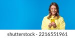 Small photo of Close-up portrait silly beautiful blond european woman in yellow hoodie, smiling at mobile phone display as watching lovely video, messaging with boyfriend, standing blue background.
