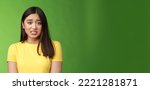 Small photo of Anxious worried cute asian girl brunette clench teeth frowning shaking from fear look guilty afraid, stand nervous awaiting punishment, green background, apologizing ashamed. Copy space