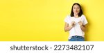 Small photo of Young asian woman in casual white t-shirt showing plastic credit card and pucker lips silly, going on shopping, yellow background.